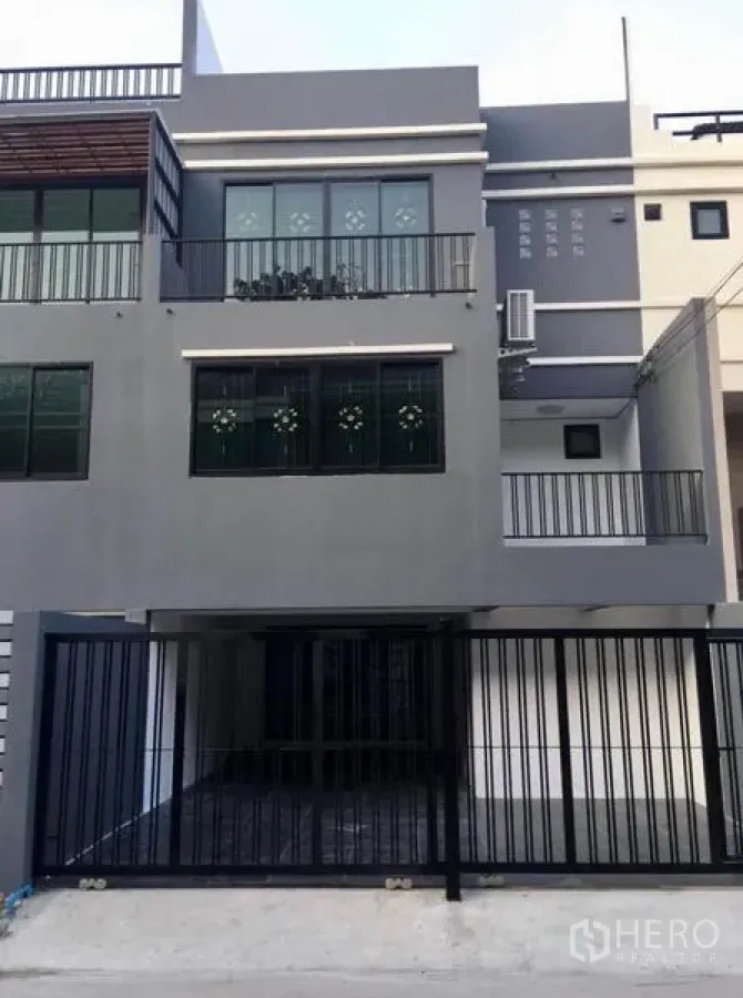 联排别墅 出租在Wang Thonglang, Bangkok - 三层灰色联排别墅外立面，带阳台与黑色庭院大门车位。