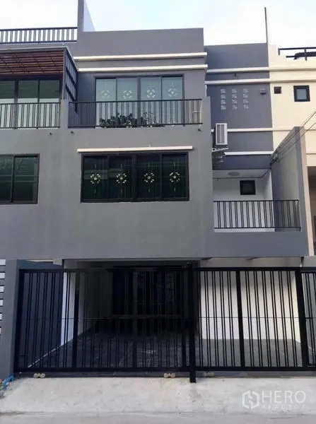 联排别墅 出租在Wang Thonglang, Bangkok - 三层灰色联排别墅外立面，带阳台与黑色庭院大门车位。