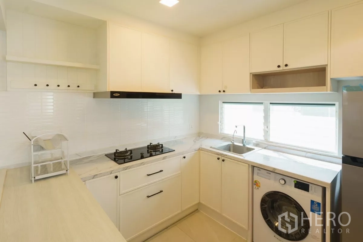 Detached House for rent in Bang Phli, Samut Prakan - U-shaped white kitchen with gas hob, sink, cabinets and washer.