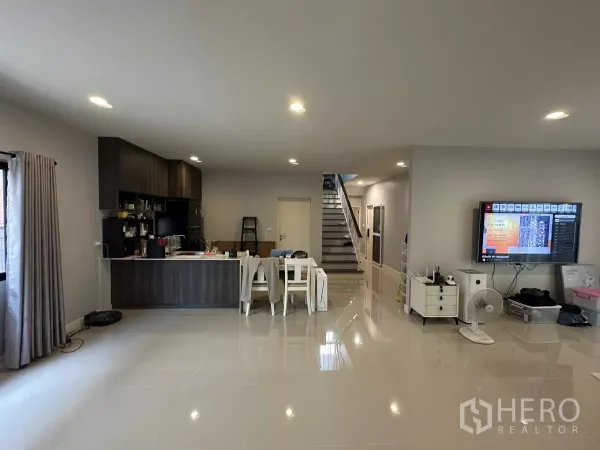 Detached House for rent or sale in Lam Luk Ka, Pathum Thani - Open-plan zone with pantry kitchen, dining table and staircase, finished with polished tiles and built-in cabinetry.