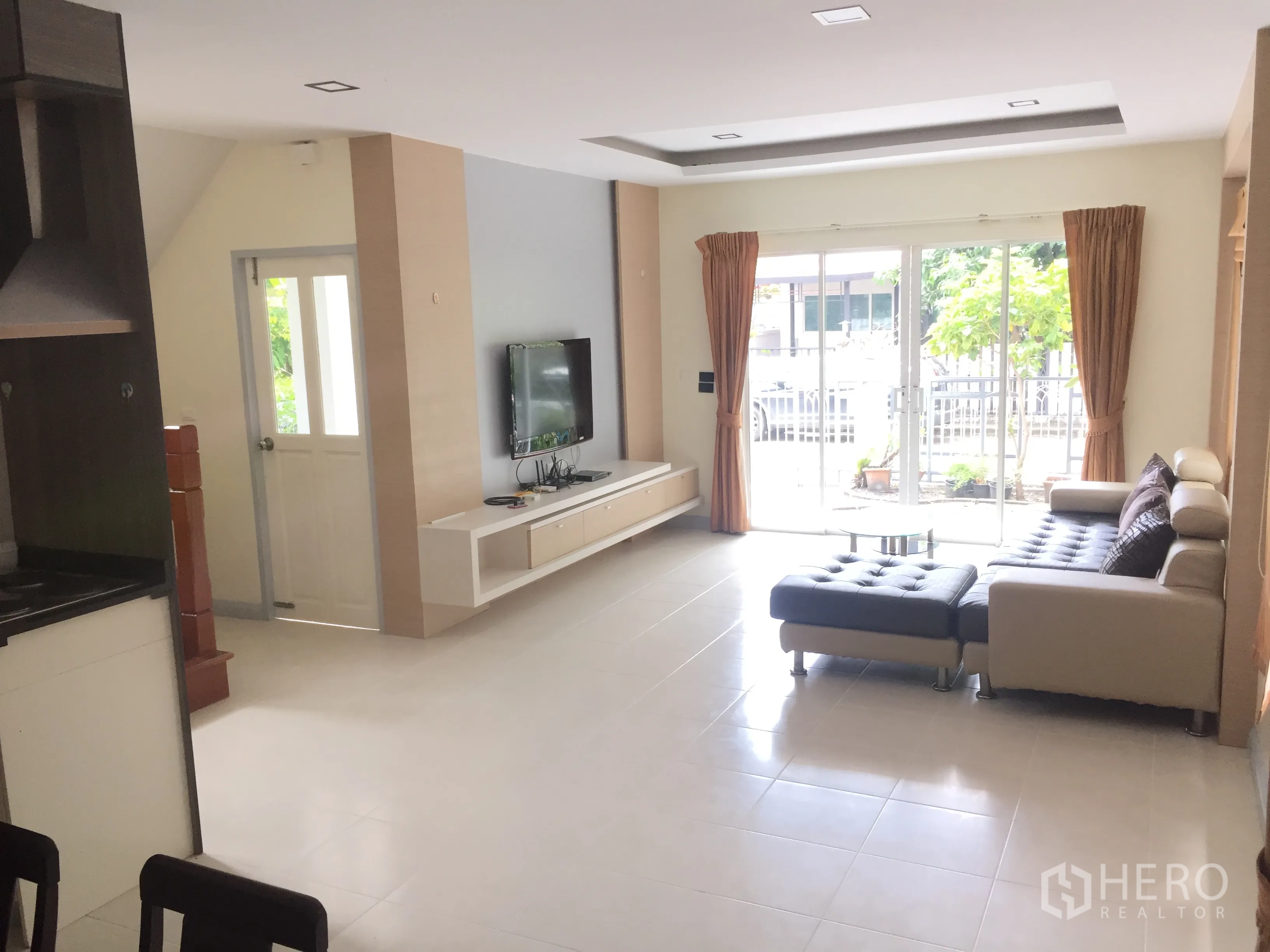 Detached House for sale in Lat Krabang, Bangkok - Bright living room with TV wall unit, L-shaped sofa and large sliding doors to the front.