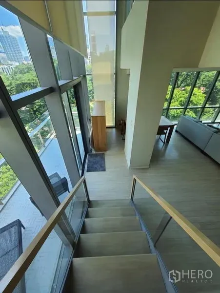 公寓 出租或出售在Watthana, Bangkok - 双层楼梯沿大面积玻璃墙通往阳台，可见城市与树梢景观，临近Asok