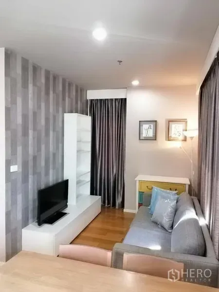 Condominium for rent in Watthana, Bangkok - Cozy living room with TV unit, feature wall and sofa beside full-length curtains