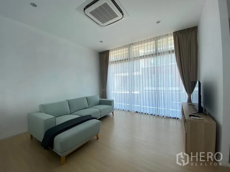Townhouse for rent in Saphan Sung, Bangkok - Airy living room with large windows, cassette air-conditioner, sofa and media console.