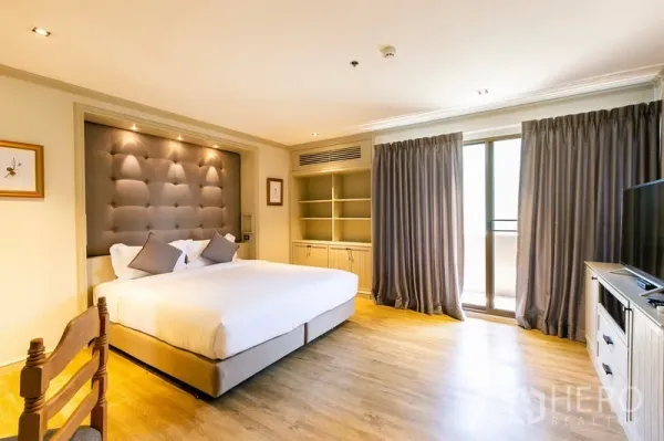 Apartment for rent in Khlong Toei, Bangkok - Sunlit master bedroom with balcony access, built-in shelves, and full-length curtains.
