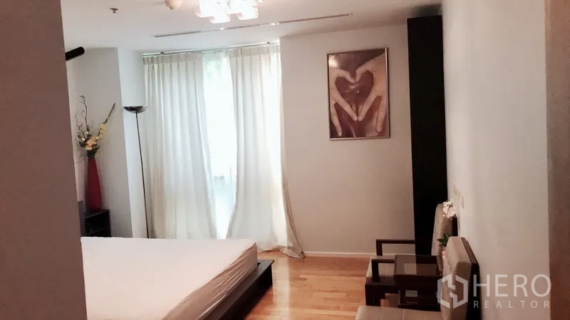 Condominium for rent in Bang Rak, Bangkok - Secondary bedroom with platform bed, soft drapes and seating by the window.