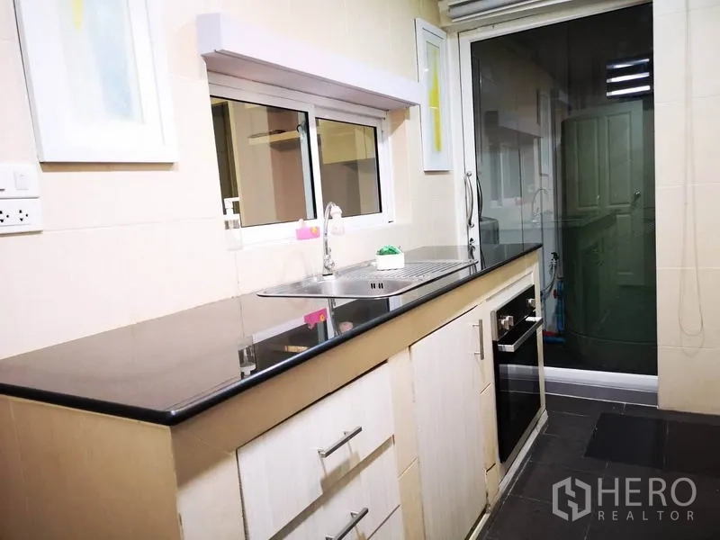Townhouse for rent in Suan Luang, Bangkok - Light kitchen with black granite countertop, sink and sliding door to utility area.