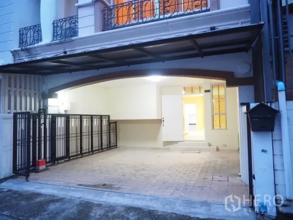 Townhouse for rent in Lat Phrao, Bangkok - Covered carport with black metal gates and tiled driveway leading to the townhouse entrance.