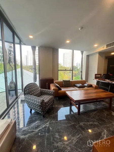 公寓 出租在Watthana, Bangkok - 转角客厅，窗外绿意与城市景色，皮沙发搭配大理石地面