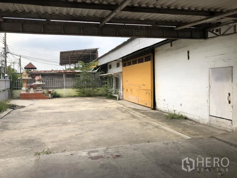 คลังสินค้า ให้เช่าในSai Mai, Bangkok - ลานคอนกรีตมีกันสาดและประตูม้วนสีเหลืองขนาดใหญ่ของโกดังย่านสายไหม