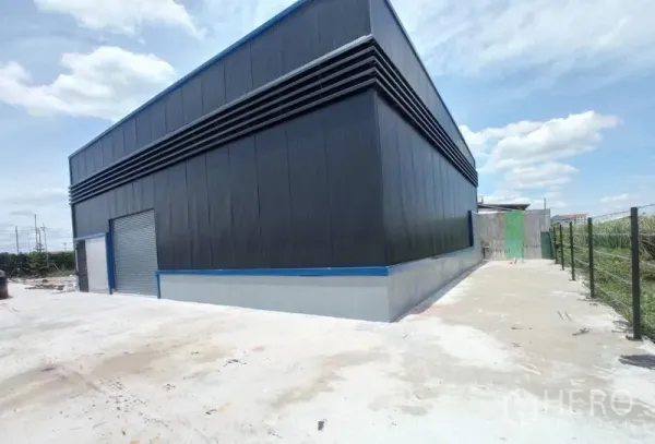 Warehouse for rent in Saphan Sung, Bangkok - Side and rear view of the warehouse with ventilation louvres and paved access road along the fence.