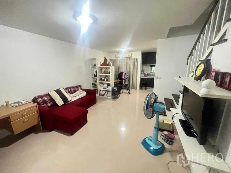 Townhouse for rent in Bueng Kum, Bangkok - Open-plan living room with red sofa, TV wall and staircase.
