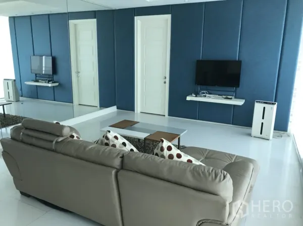 公寓 出租在Watthana, Bangkok - 蓝色软包电视墙、整面镜子与沙发的采光明亮客厅。