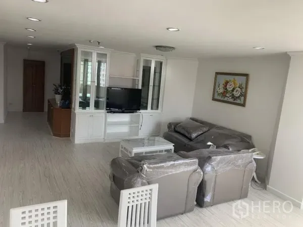 公寓 出租在Watthana, Bangkok - 明亮的开放式客厅，灰色沙发组，白色电视柜，浅色木地板与筒灯。