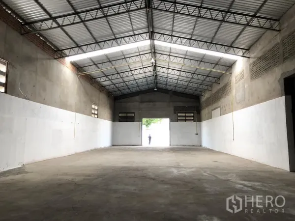 Warehouse for rent in Mueang Pathum Thani, Pathum Thani - Open warehouse hall facing the entrance, showing long LED strip lighting and smooth floor.