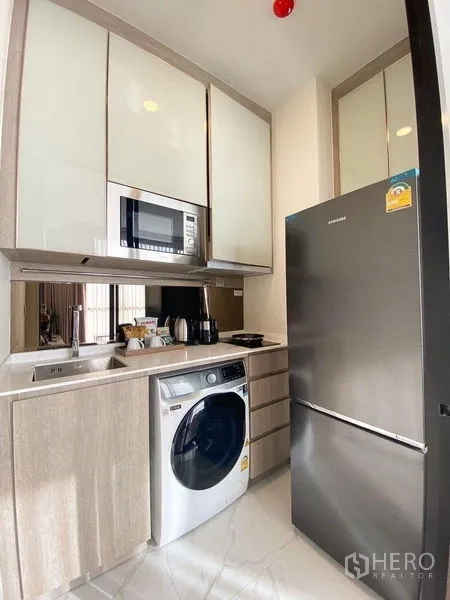 公寓 出租在Ratchathewi, Bangkok - 厨房另一角，带不锈钢大冰箱、嵌入式微波炉与石材台面。