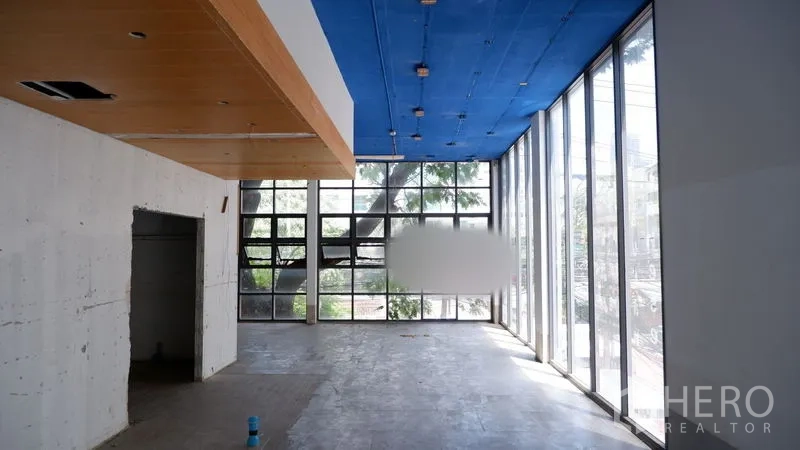 Retail Space for rent in Watthana, Bangkok - Spacious retail unit with full-height windows on two sides, concrete flooring, and tree views.