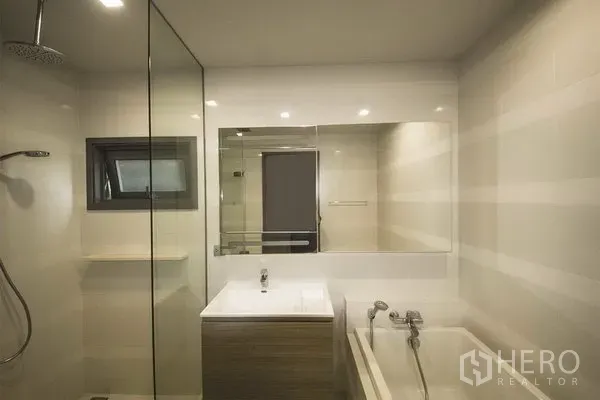Condominium for rent in Khlong Toei, Bangkok - Modern bathroom with glass shower, bathtub, large mirror and vanity in a Bangkok condo.