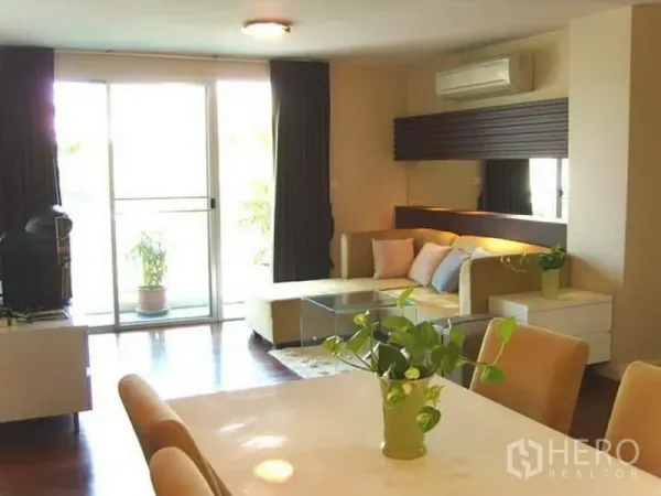公寓 出租在Watthana, Bangkok - 采光充足的客厅，L形沙发、玻璃茶几与通往阳台的推拉门