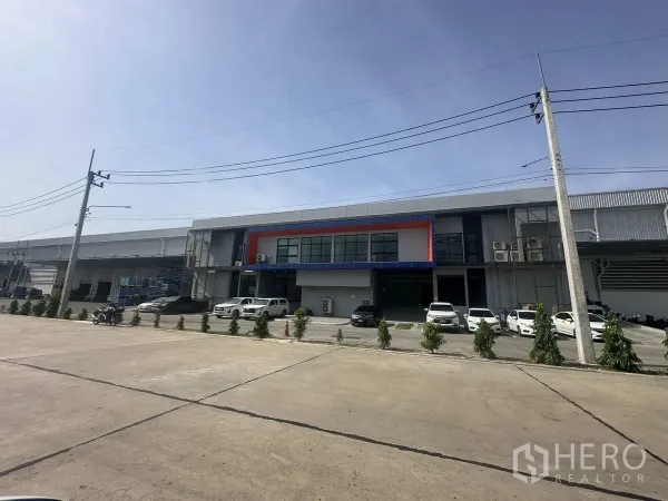 Warehouse for rent in Khlong Luang, Pathum Thani - Modern logistics warehouse facade with office frontage, parking bays, and loading areas along a wide road.