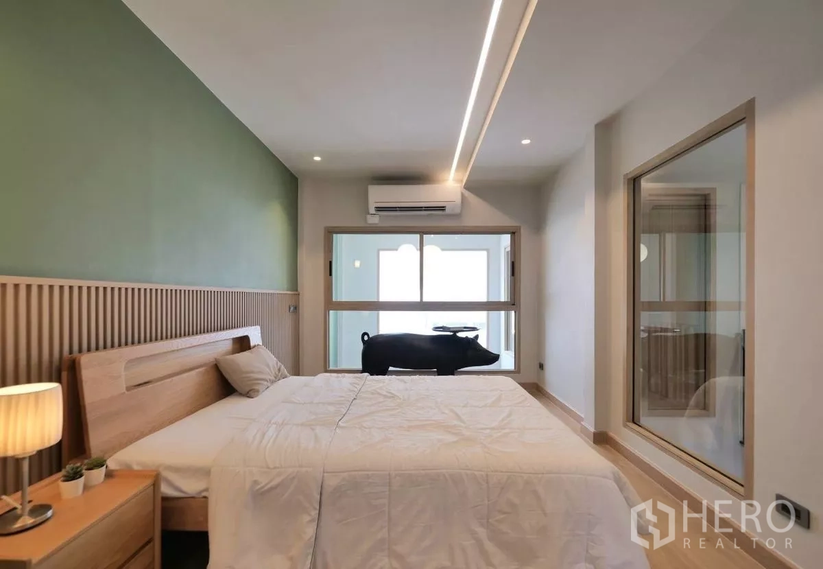 Townhouse for rent in Watthana, Bangkok - Cozy bedroom with green accent wall, wooden headboard and an internal window.
