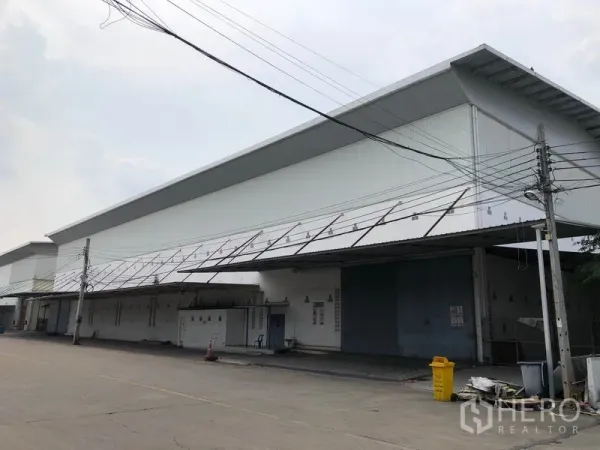 Factory for rent in Bang Bua Thong, Nonthaburi - Wide exterior of a modern white factory with long covered loading bays along a paved road.