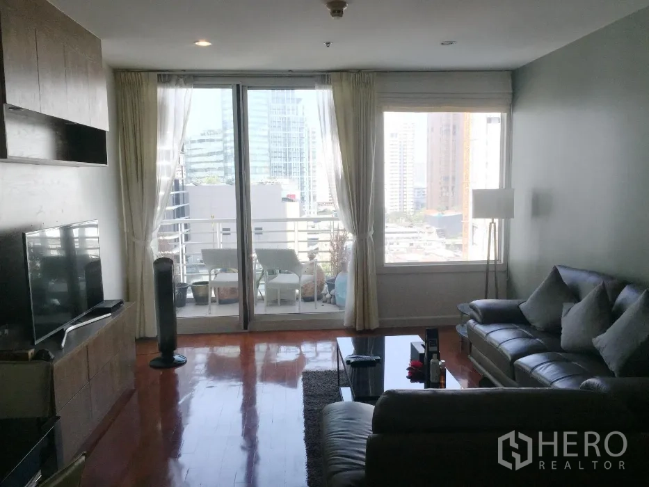 Condominium for rent or sale in Khlong Toei, Bangkok - Living area opening to a balcony with city skyline views through large sliding glass doors.