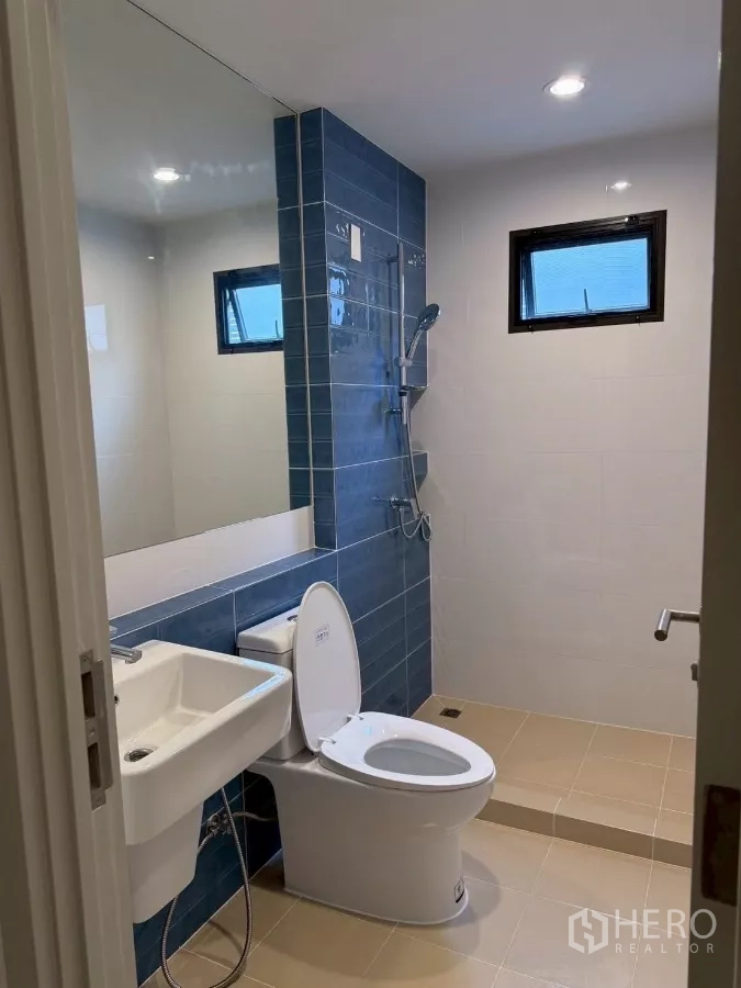 Detached House for rent in Lat Krabang, Bangkok - Bathroom with blue-tiled shower area, white basin and toilet.