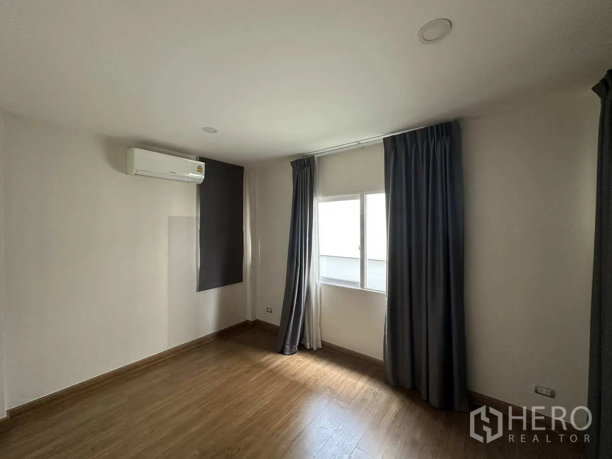 Detached House for rent in Khlong Luang, Pathum Thani - Empty bedroom with wood floors, air conditioner and curtains.