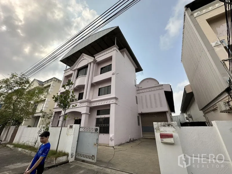 Factory for rent in Bang Bua Thong, Nonthaburi - Corner view of the factory with driveway and sliding gate on a quiet street.