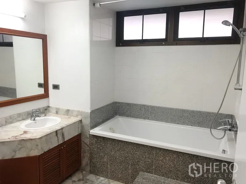 Condominium for rent or sale in Watthana, Bangkok - Bathroom with marble vanity, large built-in bathtub and upper window.