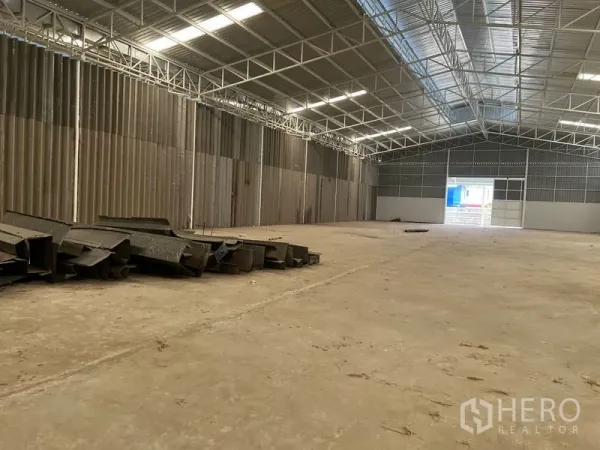 Warehouse for rent in Min Buri, Bangkok - Large warehouse bay with open loading door and stacked steel sections on the floor.