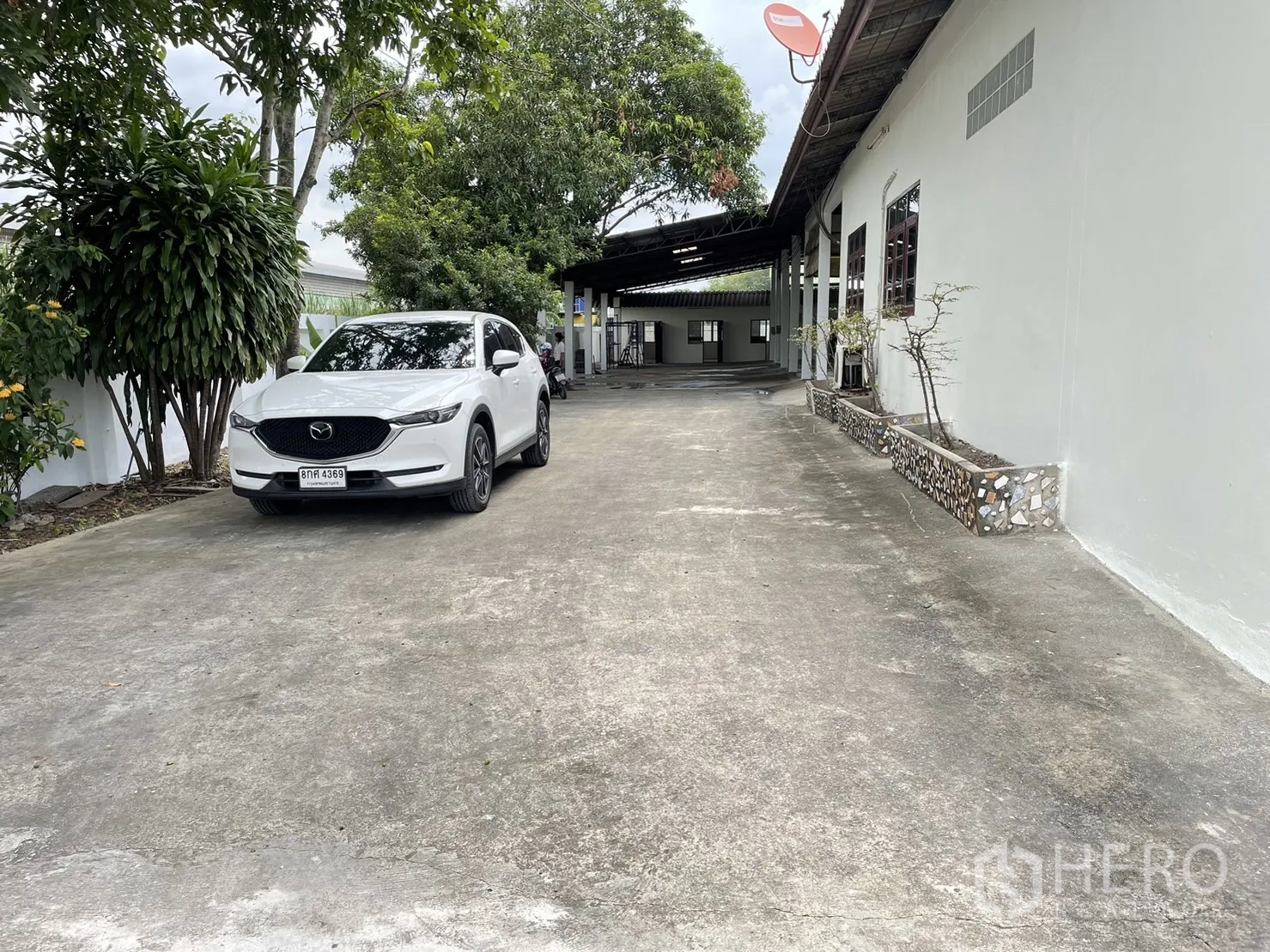 工厂 出租或出售在Pathum Thani - 长车道上停放一辆白色SUV，旁为工厂与绿化槽。