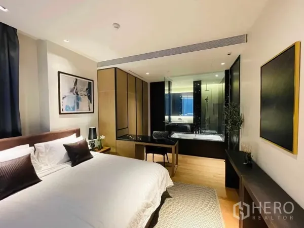 Condominium for rent in Khlong Toei, Bangkok - Modern bedroom with desk, wardrobes and a glass-partition bathroom featuring a soaking tub.
