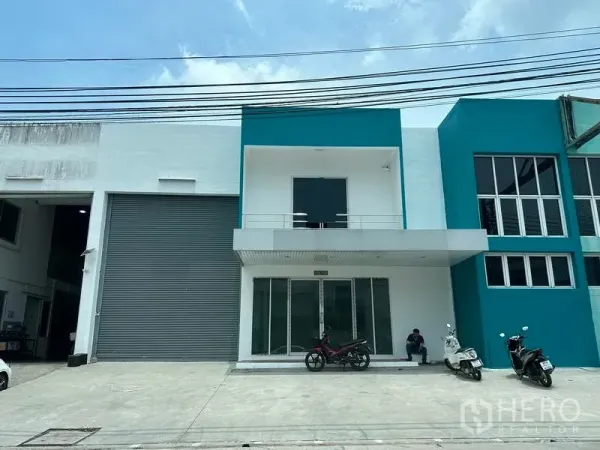 Factory for rent or sale in Samut Prakan - Modern factory exterior in Bang Phli with teal facade, glass-front office, and a large roller shutter door.