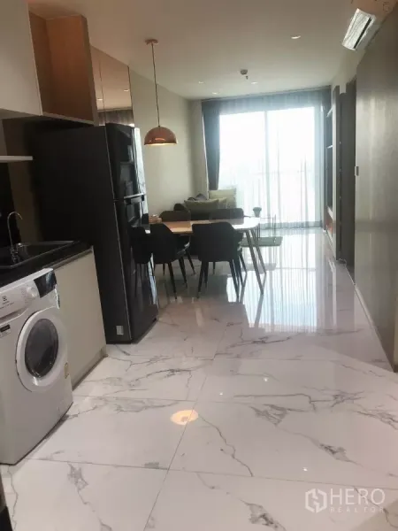 公寓 出租在Watthana, Bangkok - 大理石纹地面走廊，配置一体化厨房、冰箱与餐桌，通向明亮阳台。