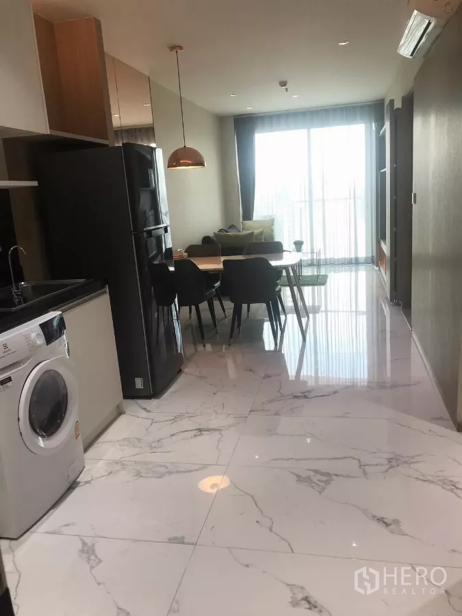 公寓 出租在Watthana, Bangkok - 大理石纹地面走廊，配置一体化厨房、冰箱与餐桌，通向明亮阳台。