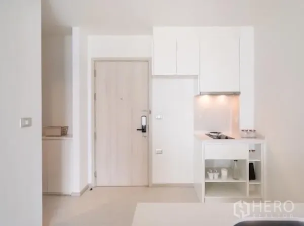 Condominium for sale in Khlong Toei, Bangkok - Minimal entry hall with light-wood door and built-in white kitchenette with cooktop and cabinets.