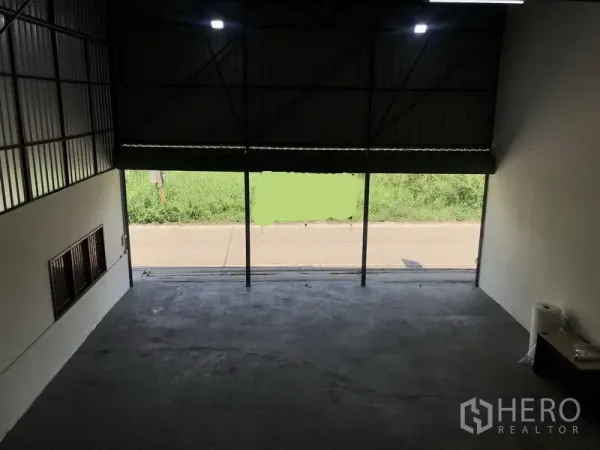 Warehouse for rent in Lam Luk Ka, Pathum Thani - View from the mezzanine toward a large roller door opening to the road and green verge.
