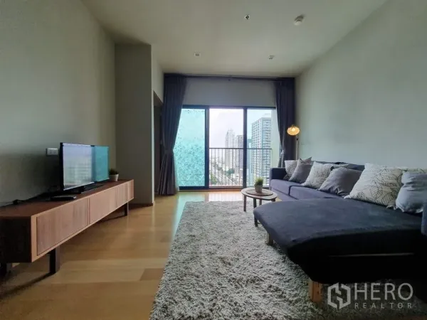 Condominium for rent in Ratchathewi, Bangkok - Spacious living room with sectional sofa, rug, TV, and large windows.