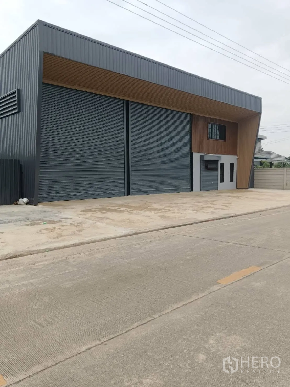 Warehouse for rent in Lam Luk Ka, Pathum Thani - Angled street view of the warehouse frontage with spacious driveway for vehicle access.
