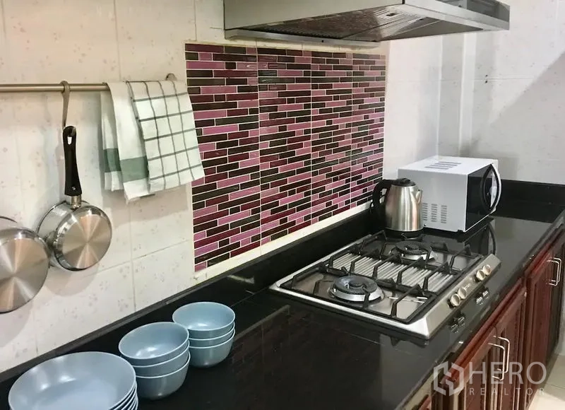 联排别墅 出租在Bang Rak, Bangkok - 厨房特写，黑色花岗岩台面，燃气灶与抽油烟机，马赛克墙面，水壶和微波炉。