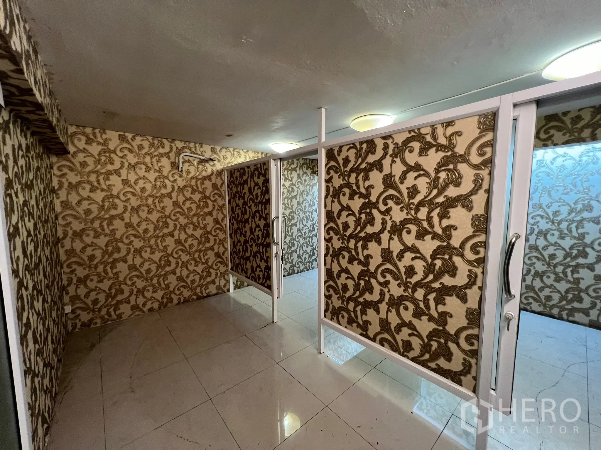 Shophouse for rent in Khlong Toei, Bangkok - Narrow retail cubicle with sliding door, white tiles and ornate wallpaper.