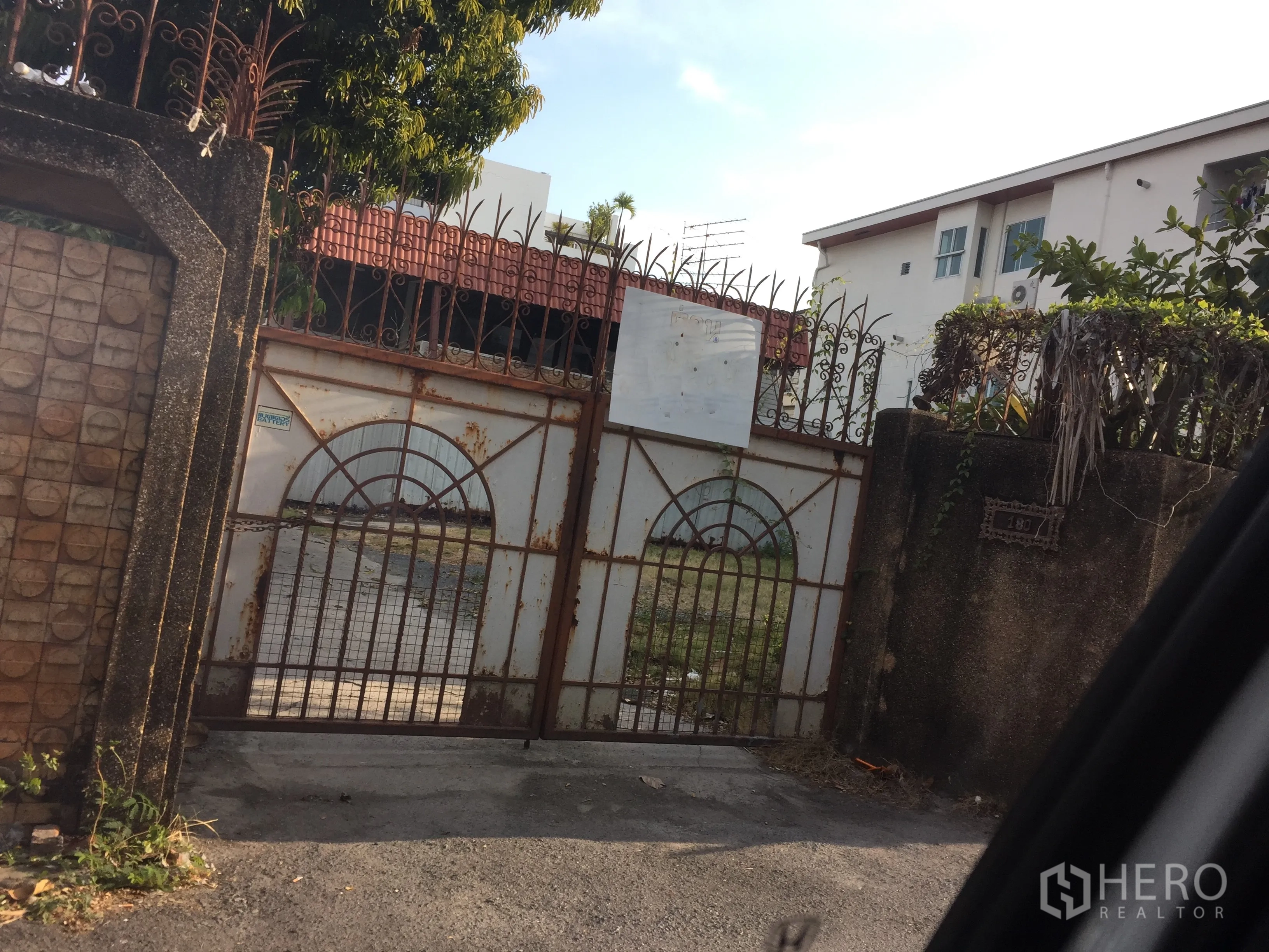 独立式住宅 出售在Watthana, Bangkok - 曼谷瓦他那区独栋别墅入口的铁艺大门与混凝土围墙，可见车道与绿植。