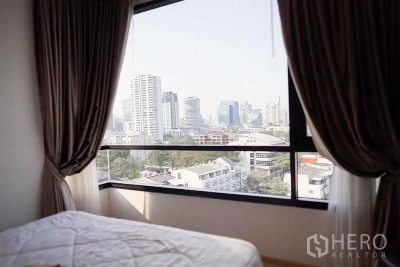 公寓 出租或出售在Watthana, Bangkok - 卧室大窗框出曼谷天际线景观，配深色遮光帘。