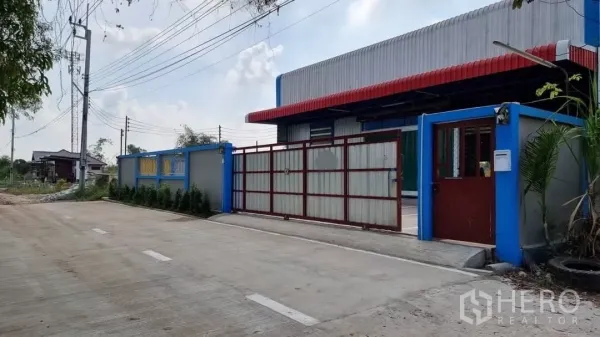 คลังสินค้า ให้เช่าในMin Buri, Bangkok - ประตูรั้วโกดังเดี่ยว พร้อมกันสาดสีแดง กำแพงทาสีฟ้า และทางเข้าถนนคอนกรีตกว้าง