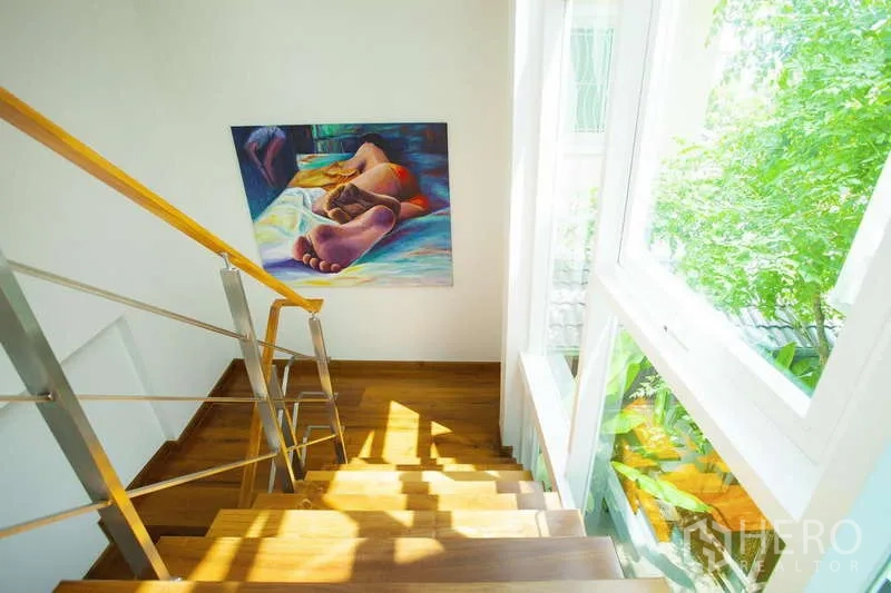 Detached House for rent in Lat Phrao, Bangkok - Sunlit staircase with wooden steps, metal handrail, and a tall window overlooking greenery.