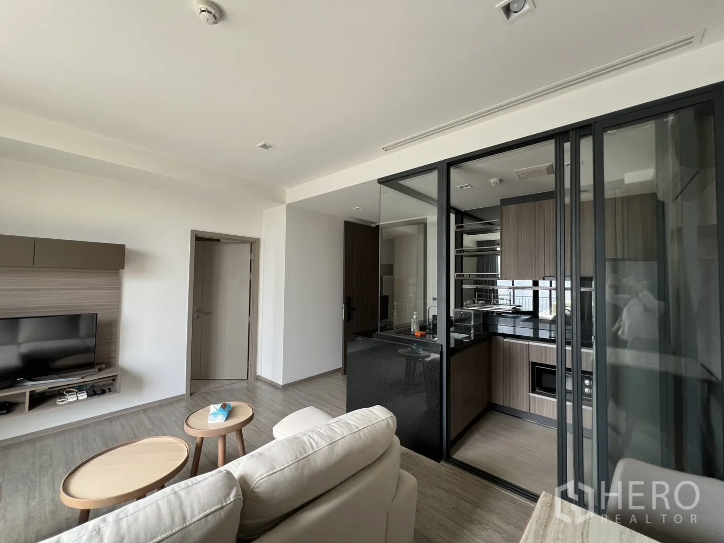 คอนโด for rent in Watthana, Bangkok - ห้องนั่งเล่นพร้อมชั้นวางทีวีติดผนัง โซฟา และทางเข้าครัวกั้นกระจก.