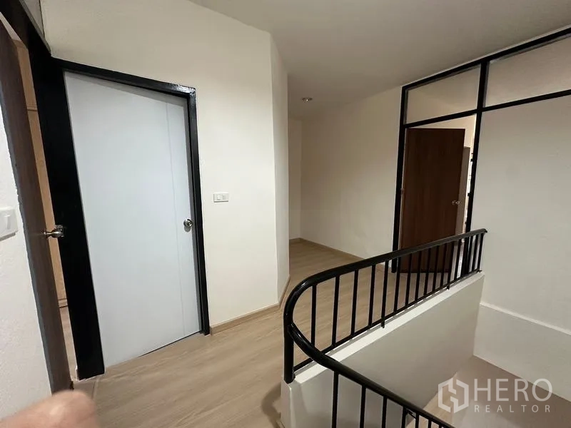 Townhouse for rent or sale in Phra Khanong, Bangkok - Upper landing with doors and black-framed glass partition.