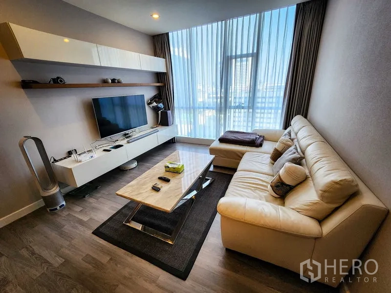 Condominium for rent or sale in Bang Rak, Bangkok - Cozy lounge with sectional sofa, TV shelf, and tall sheer curtains.